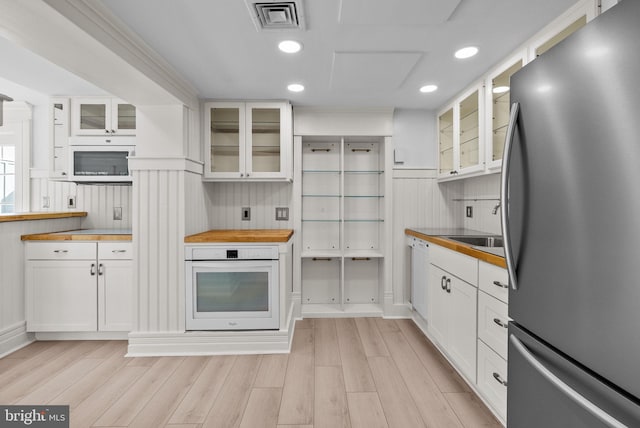 kitchen featuring wooden counters, visible vents, freestanding refrigerator, white cabinetry, and oven