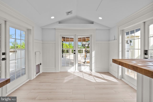 doorway to outside featuring a decorative wall, visible vents, lofted ceiling, and a wainscoted wall