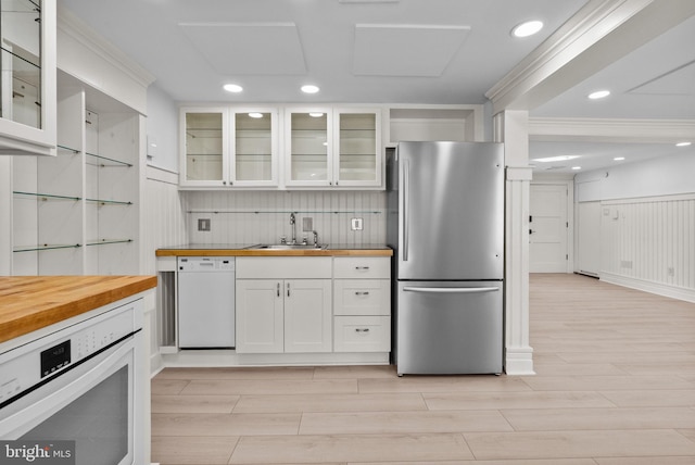 kitchen with white appliances, white cabinetry, wood counters, and a sink