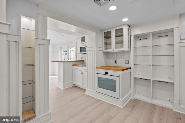 kitchen featuring glass insert cabinets, butcher block countertops, white oven, light wood-type flooring, and white cabinetry