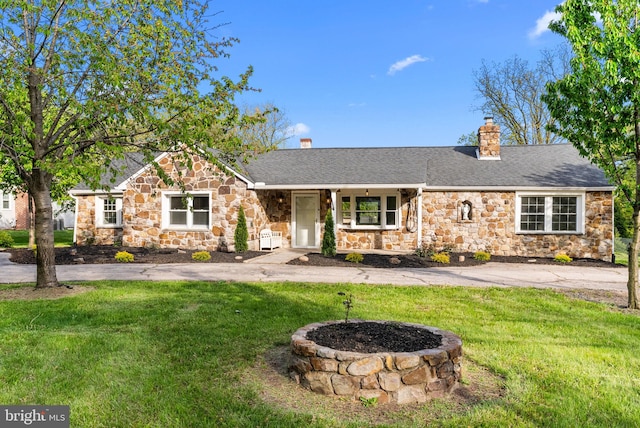 single story home featuring a chimney, a front yard, stone siding, and a porch