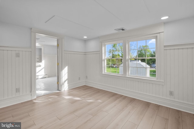 empty room with a baseboard heating unit, visible vents, wainscoting, and light wood-style flooring