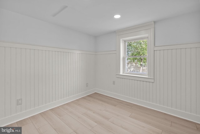 spare room with a wainscoted wall, baseboards, and light wood finished floors