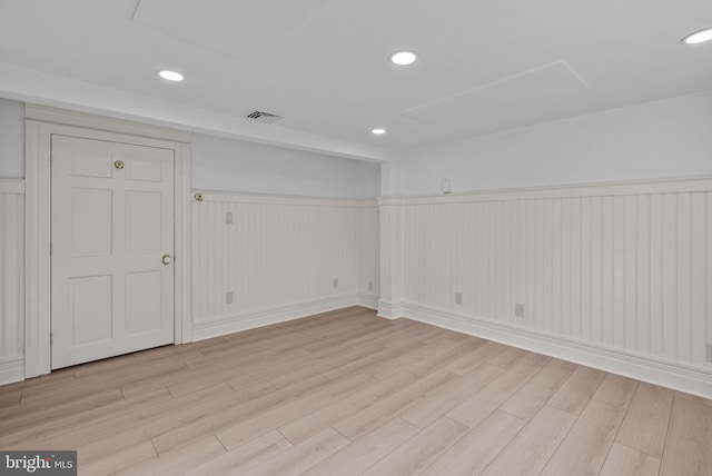 basement with light wood-style floors, recessed lighting, wainscoting, and visible vents
