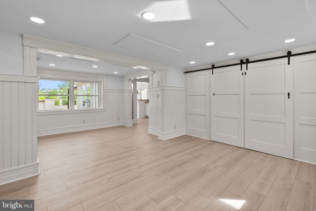 unfurnished living room featuring wainscoting, light wood-type flooring, a barn door, a decorative wall, and recessed lighting
