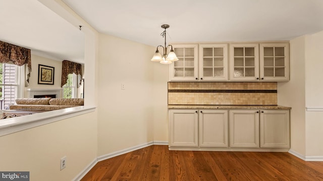 unfurnished dining area featuring a lit fireplace, baseboards, a notable chandelier, and dark wood-style floors