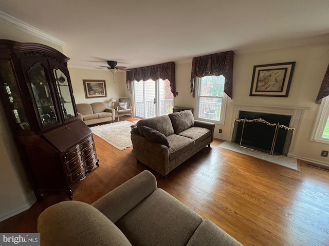 living room with ornamental molding, a fireplace with flush hearth, ceiling fan, and wood finished floors