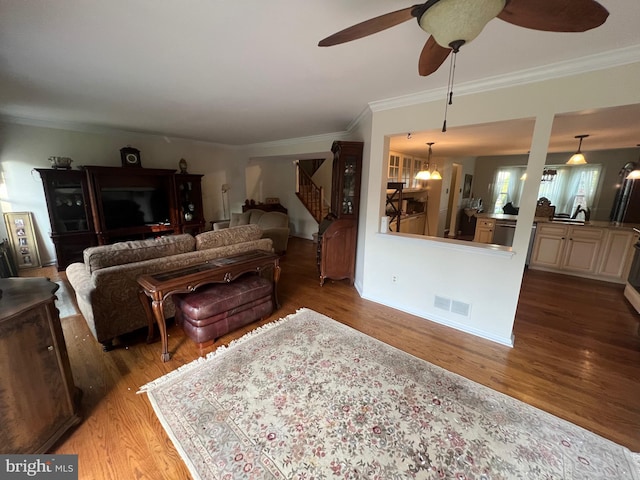 living area with visible vents, crown molding, wood finished floors, ceiling fan, and stairway