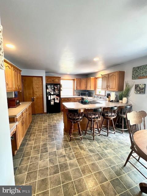 kitchen with freestanding refrigerator, a peninsula, a breakfast bar, light countertops, and stainless steel microwave