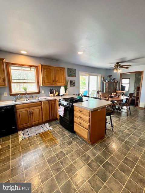 kitchen with a peninsula, light countertops, dark tile patterned flooring, a sink, and black appliances