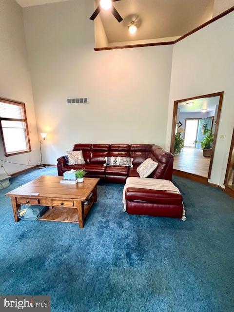 living area with ceiling fan, carpet, a high ceiling, and visible vents