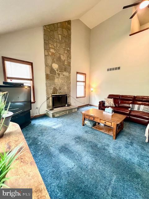 carpeted living room featuring high vaulted ceiling, ceiling fan, a stone fireplace, and visible vents