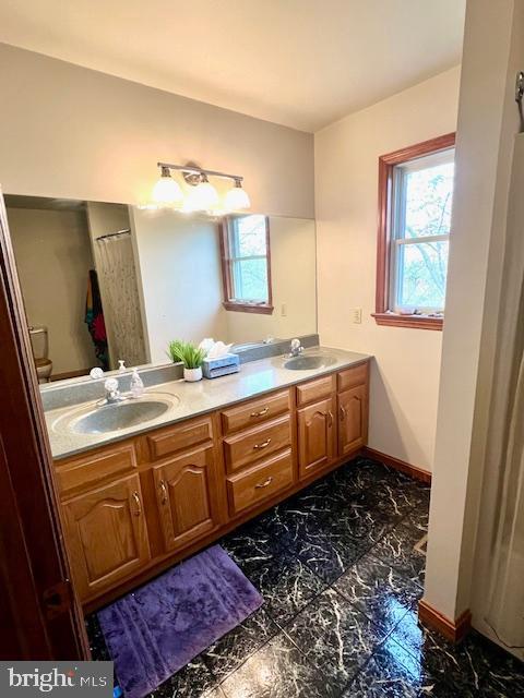 full bath with a sink, a wealth of natural light, and marble finish floor