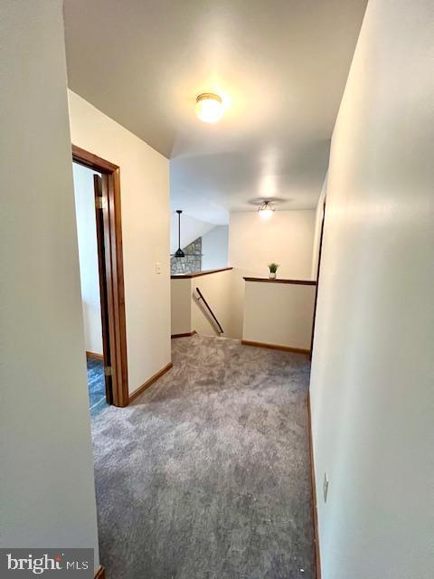 hall with baseboards, carpet, vaulted ceiling, and an upstairs landing