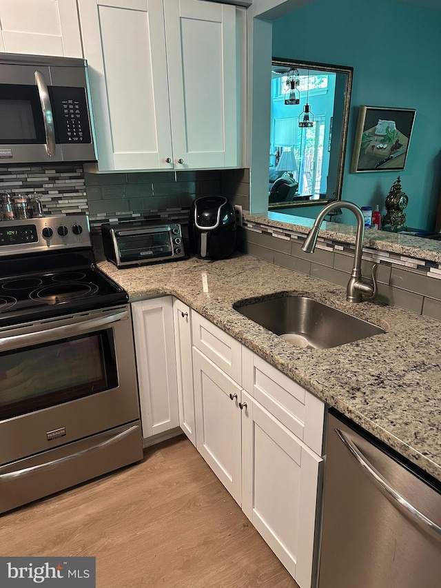 kitchen featuring appliances with stainless steel finishes, a sink, white cabinets, and light wood-style flooring