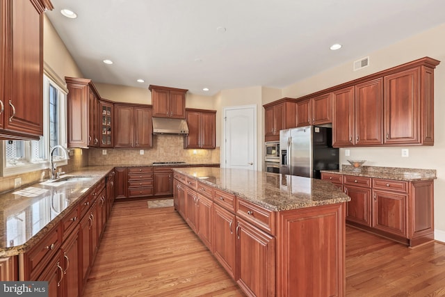 kitchen with a center island, light wood-type flooring, under cabinet range hood, a sink, and appliances with stainless steel finishes