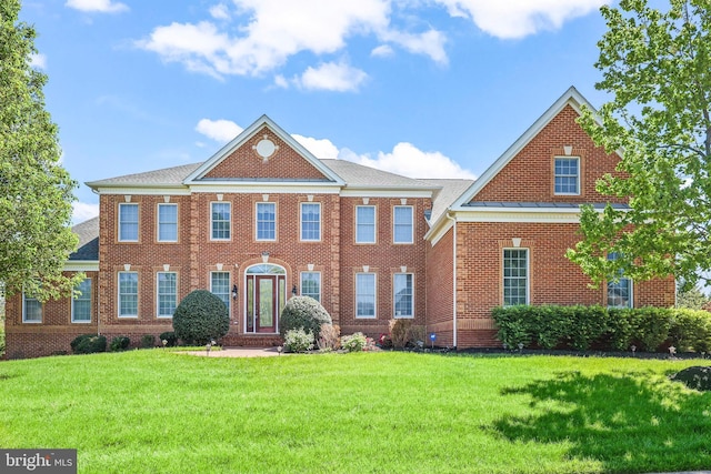colonial inspired home featuring brick siding, a shingled roof, and a front lawn