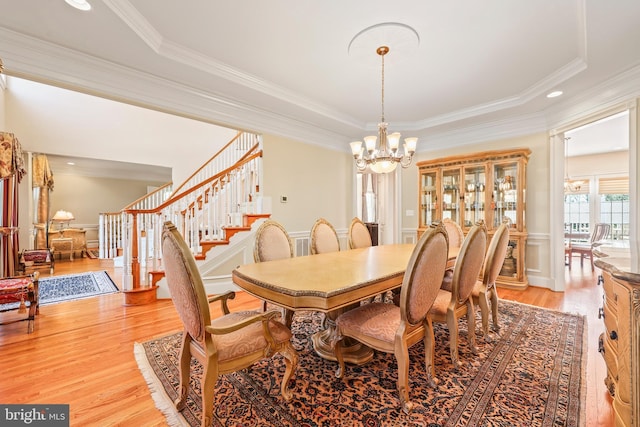 dining space featuring crown molding, a tray ceiling, a notable chandelier, and light wood-style flooring