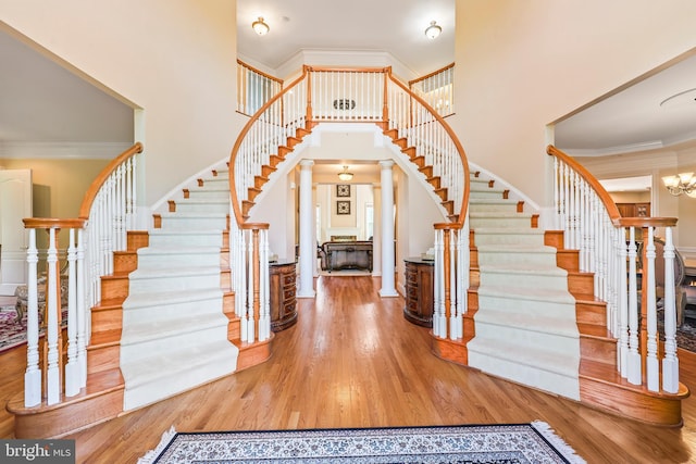 foyer featuring a high ceiling, an inviting chandelier, stairs, decorative columns, and wood finished floors