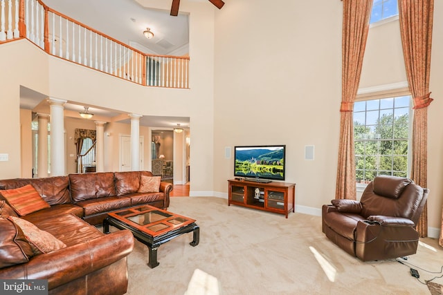 carpeted living area featuring ornate columns, baseboards, a healthy amount of sunlight, and a towering ceiling