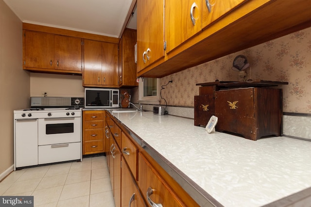 kitchen with brown cabinets, a sink, white gas stove, wallpapered walls, and stainless steel microwave