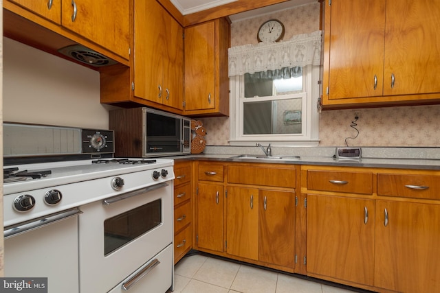 kitchen with brown cabinetry, a sink, white range with gas stovetop, and light tile patterned flooring