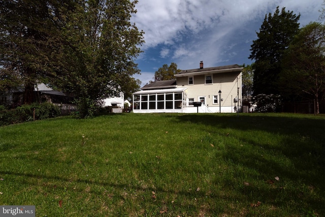 back of property featuring a lawn, a chimney, and a sunroom