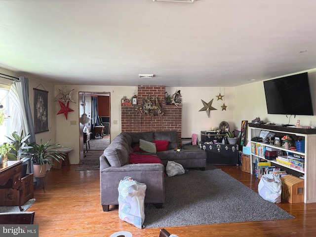 living area with a brick fireplace, visible vents, and wood finished floors