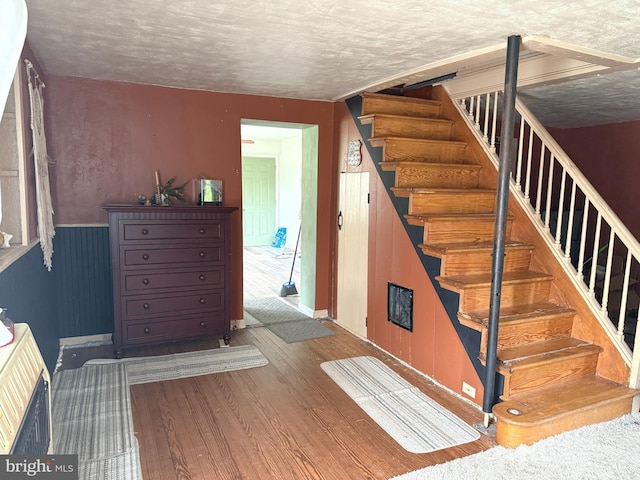 stairway with a textured ceiling, baseboards, and wood finished floors