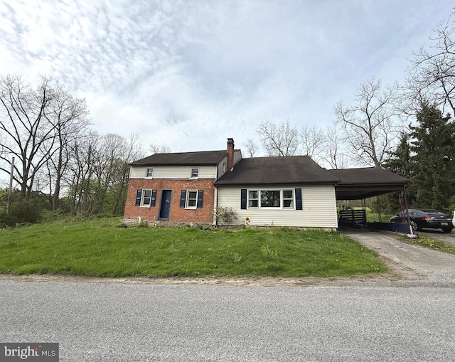 view of front of home with driveway, a chimney, a front yard, a carport, and brick siding
