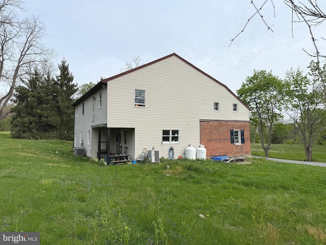 rear view of house featuring a lawn, central AC, and brick siding