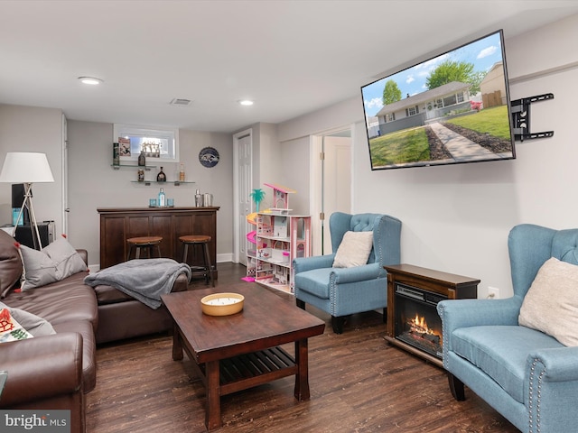 living area with visible vents, a glass covered fireplace, wood finished floors, recessed lighting, and bar