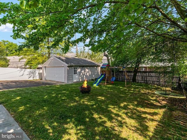 view of yard with a detached garage, a fenced backyard, an outbuilding, a playground, and a fire pit