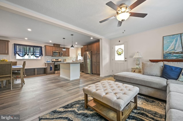 living room featuring recessed lighting, ceiling fan, ornamental molding, and light wood-style floors