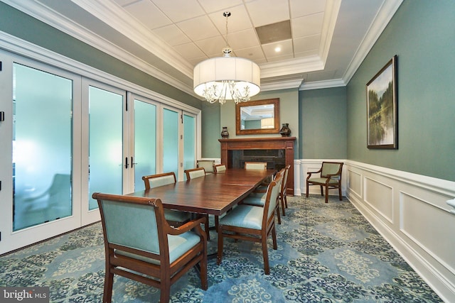 dining room featuring crown molding, a decorative wall, a raised ceiling, french doors, and a notable chandelier
