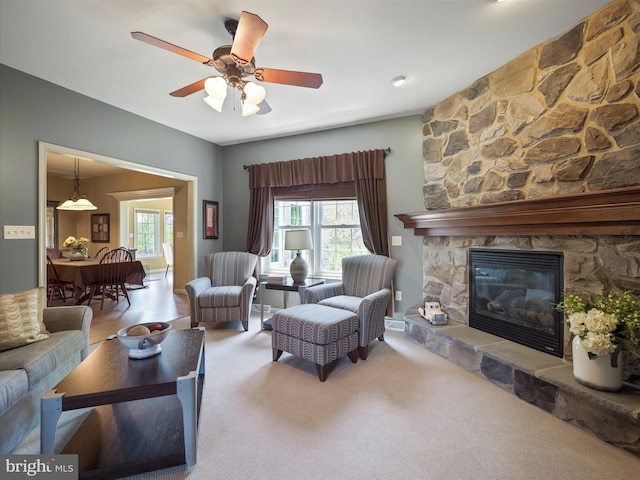 living area with carpet floors, ceiling fan, and a stone fireplace