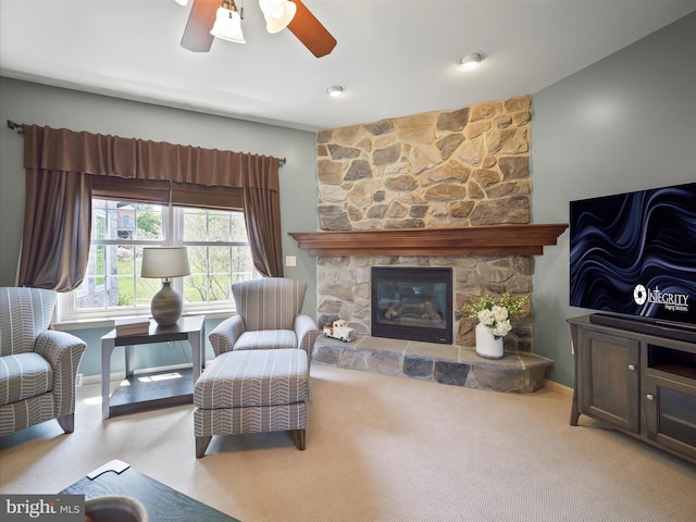 living room featuring a ceiling fan, baseboards, a stone fireplace, and carpet