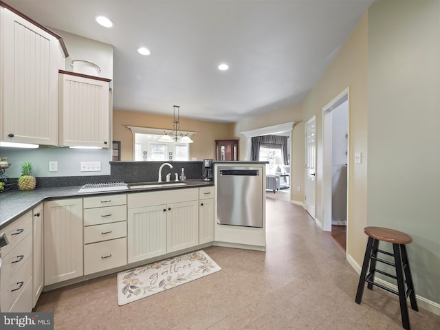 kitchen featuring stainless steel dishwasher, a sink, a peninsula, and dark countertops