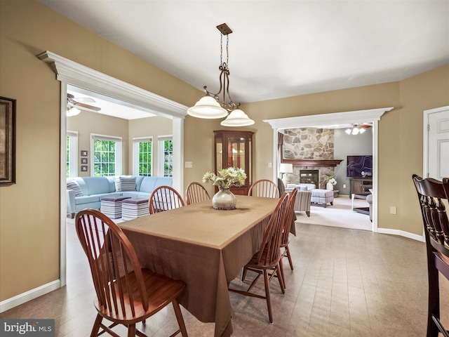 dining room featuring baseboards, ceiling fan, a stone fireplace, and wood finished floors