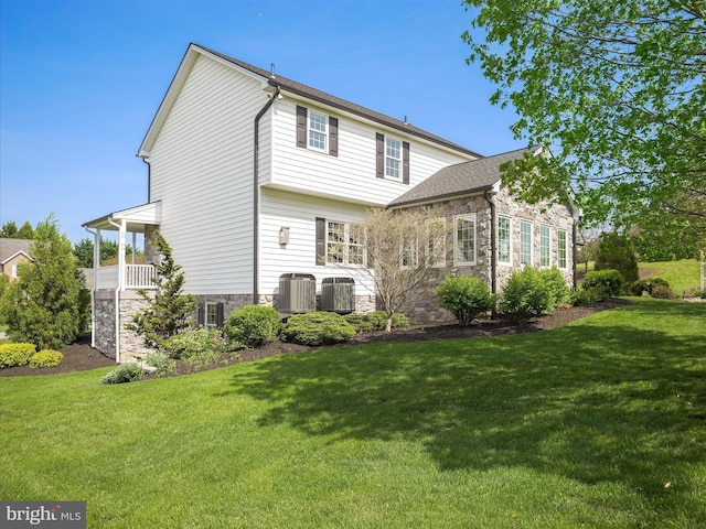 rear view of property with central AC unit, a yard, and stone siding