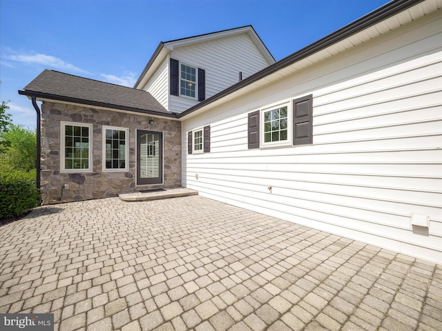 rear view of house featuring a patio area and stone siding