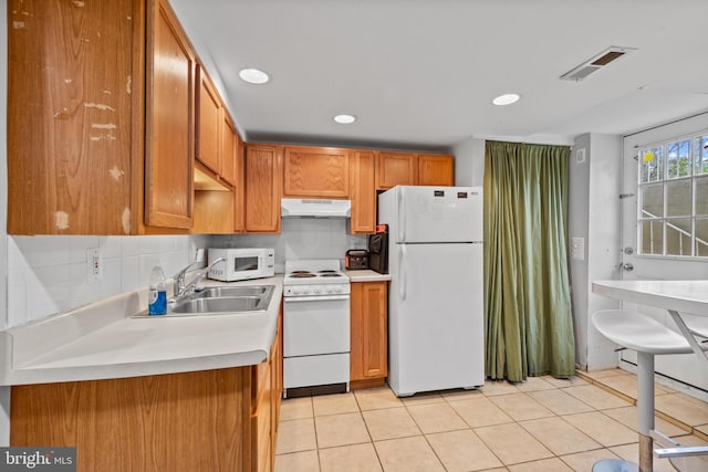 kitchen with a sink, light countertops, under cabinet range hood, white appliances, and light tile patterned flooring