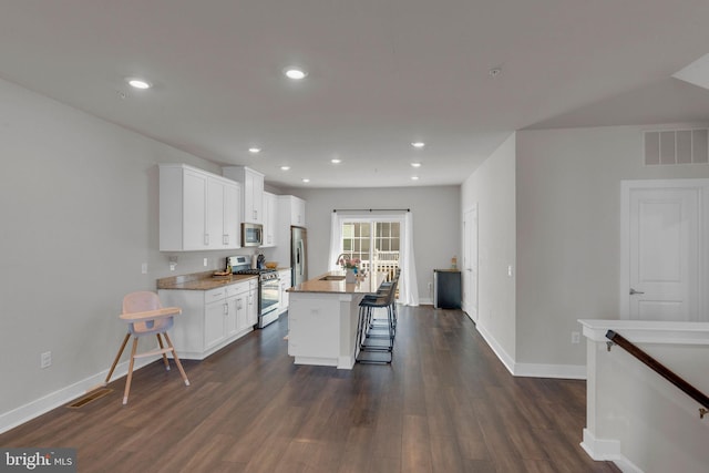 kitchen featuring visible vents, baseboards, a breakfast bar area, dark wood finished floors, and stainless steel appliances