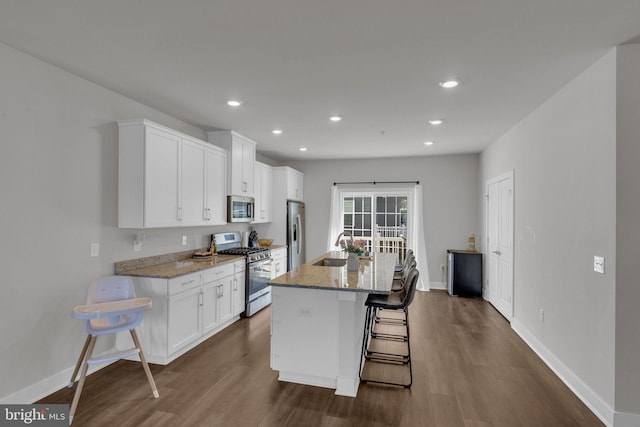 kitchen featuring a kitchen breakfast bar, white cabinets, dark wood-type flooring, stainless steel appliances, and an island with sink