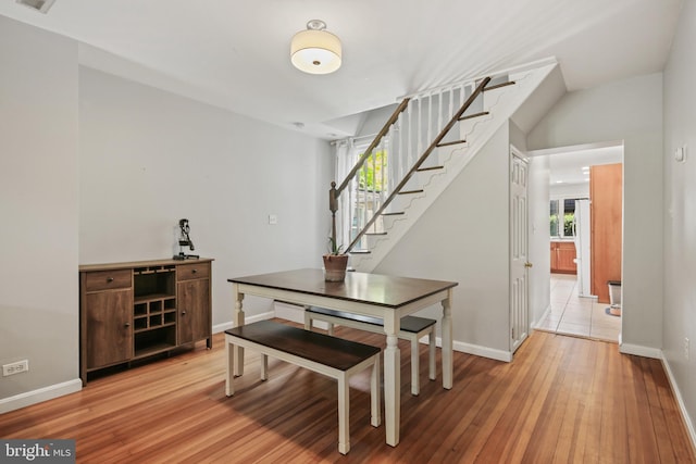 dining space featuring baseboards, light wood finished floors, and stairway