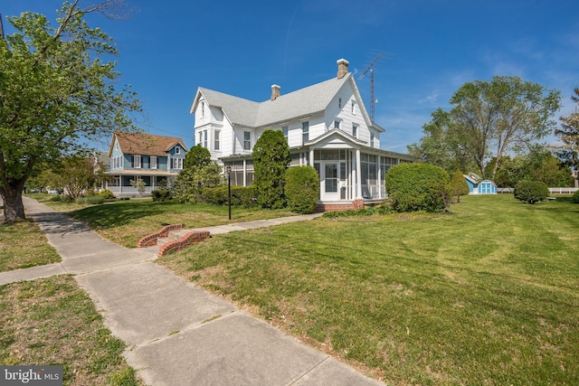 view of front of house with a front yard, a chimney, a shingled roof, and a sunroom