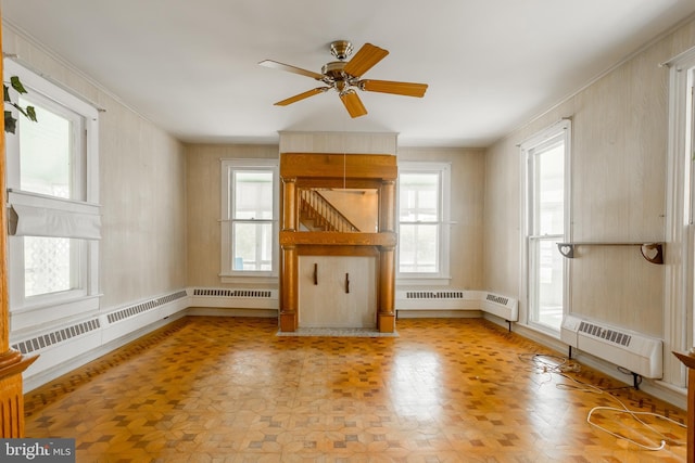 unfurnished living room featuring a healthy amount of sunlight, ceiling fan, and a baseboard heating unit