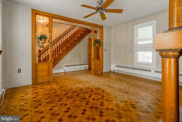 unfurnished living room featuring stairs, a baseboard heating unit, ceiling fan, and decorative columns