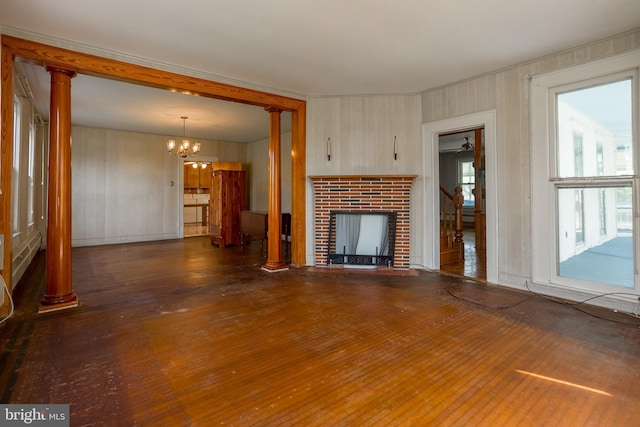 unfurnished living room featuring ornate columns, a notable chandelier, wood finished floors, and a fireplace