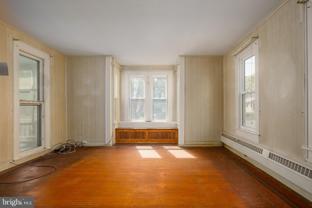empty room featuring radiator heating unit, a baseboard radiator, wood-type flooring, and a healthy amount of sunlight
